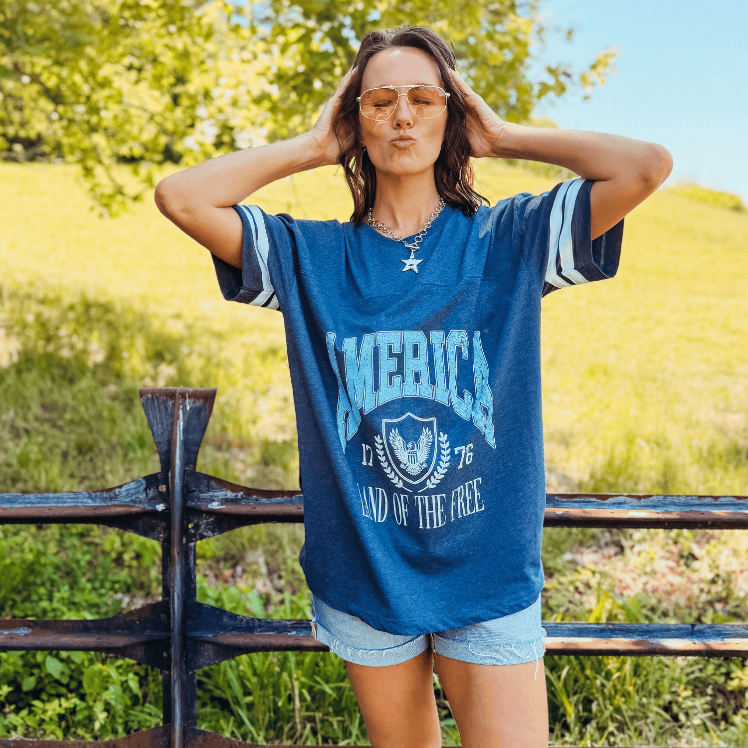 Land of the Free jersey tee in navy blue with white stripes, featuring a graphic print and model posing outdoors.