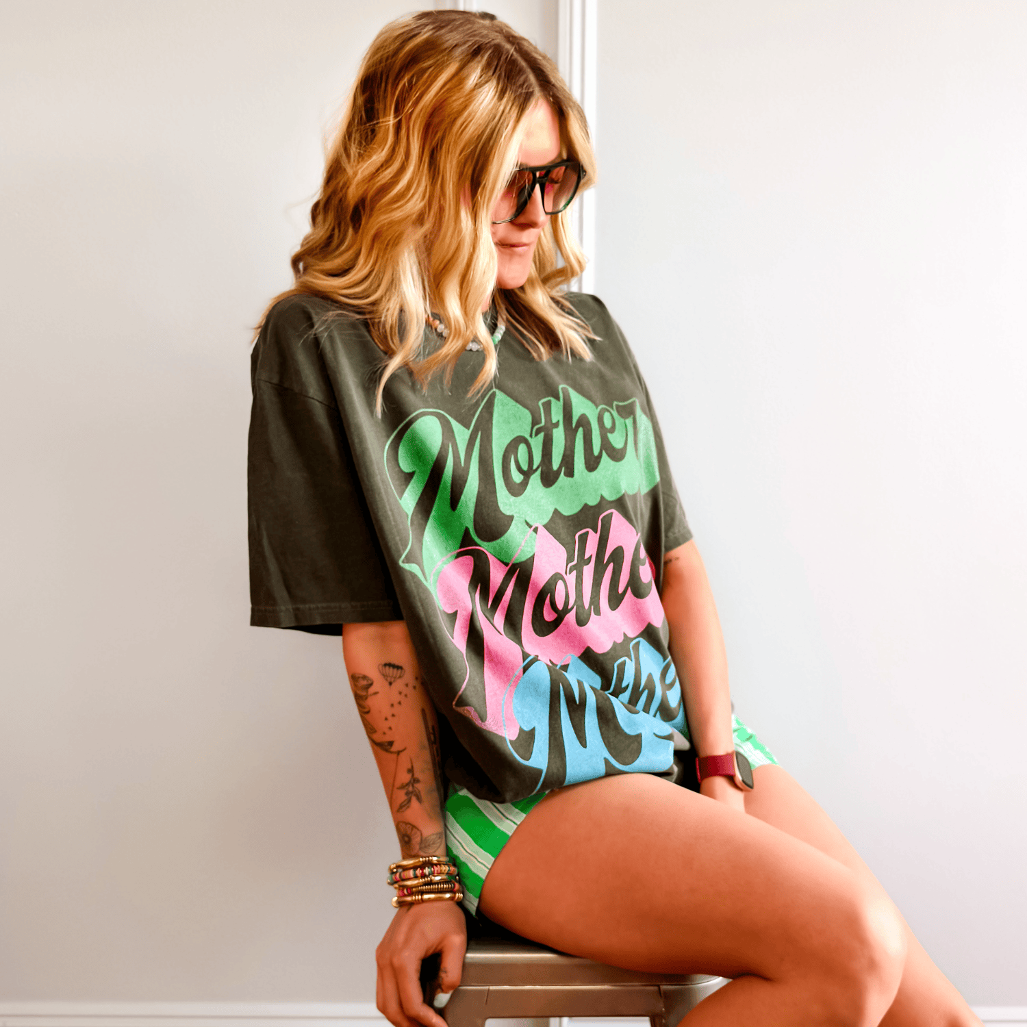 Person wearing a graphic t-shirt with colorful text sitting on a chair.