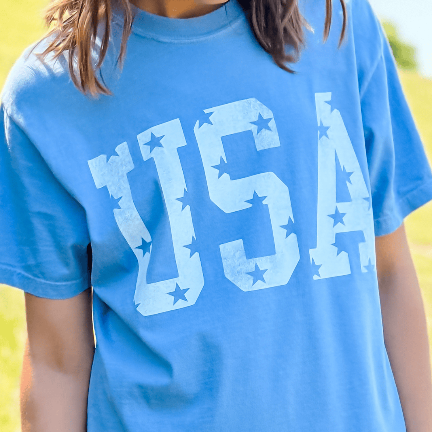 Distressed USA tee in washed denim blue with white star and letter print, worn by a model outdoors.