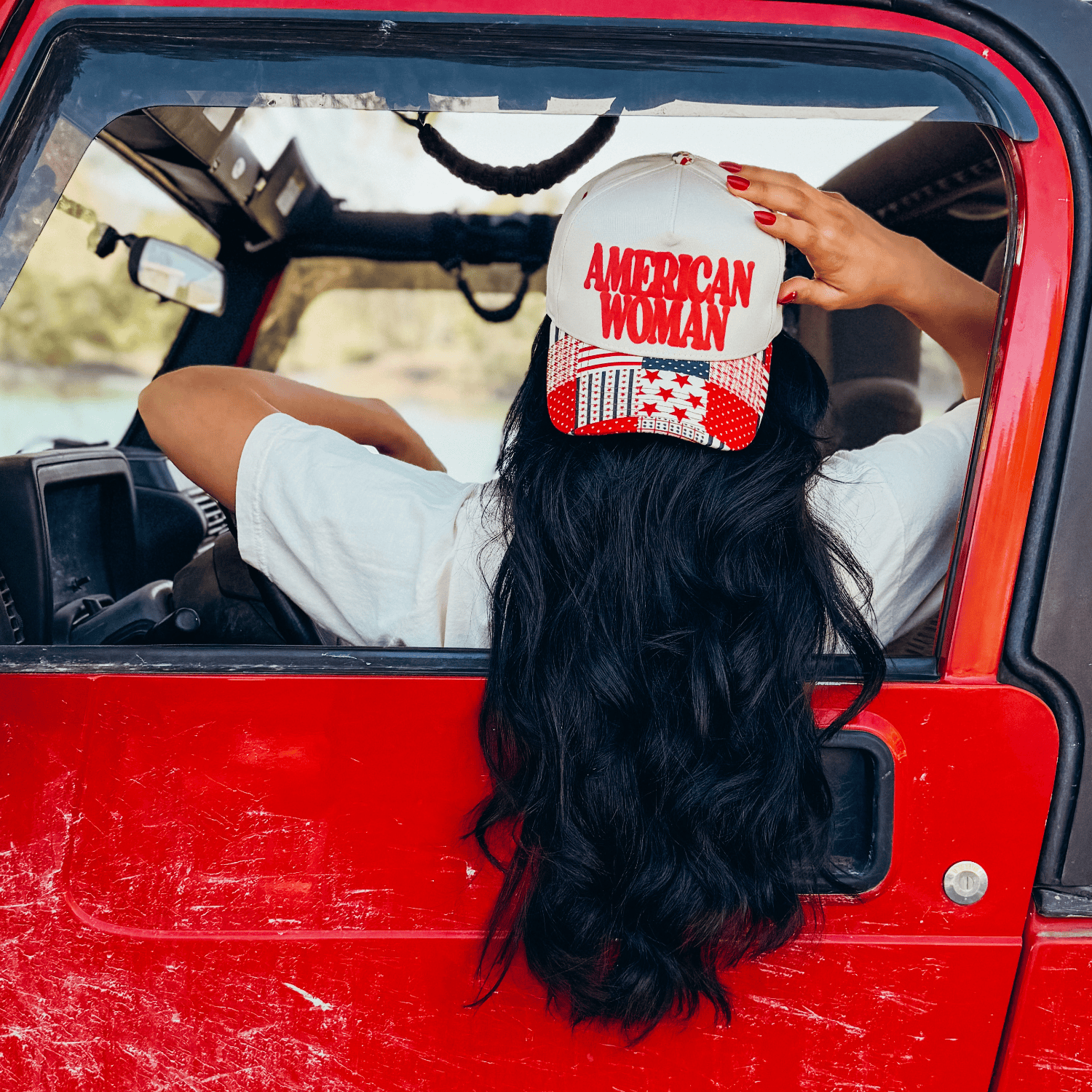 American Woman puff pattern hat worn by a woman with long black hair, seated in a red vehicle.