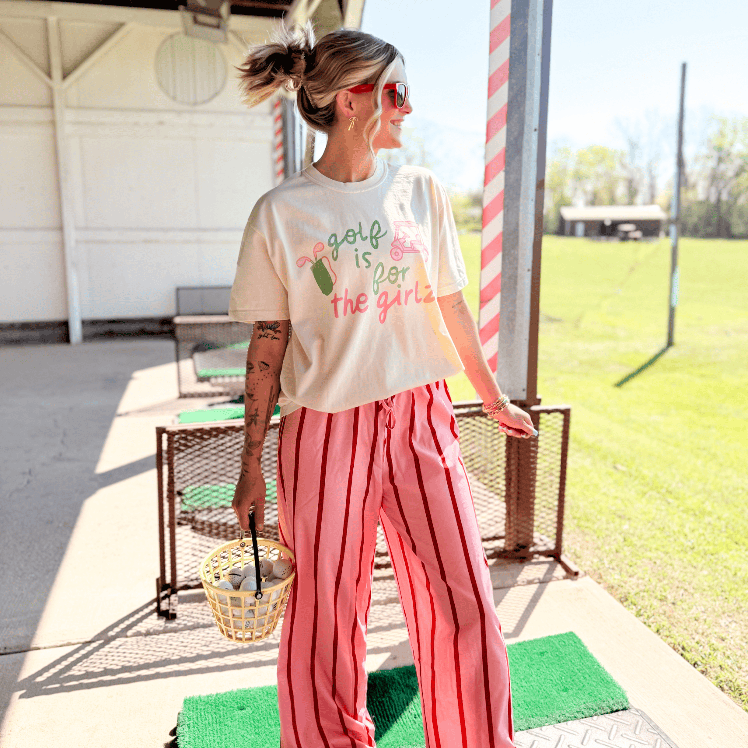 Woman wearing a t-shirt with text and pink pants standing on a golf green.
