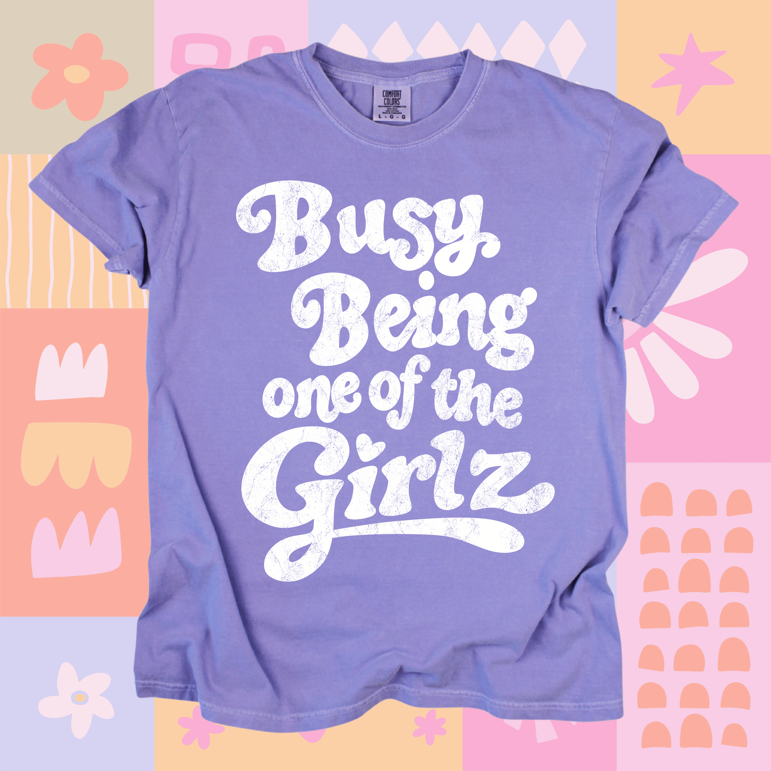 Purple t-shirt with 'Busy Being one of the Girlz' text on a colorful patterned background