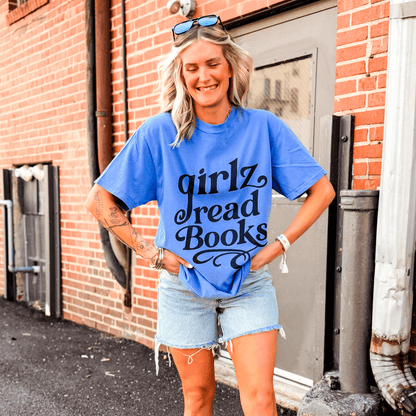 Blue Girlz Read Books tee worn by a smiling woman, paired with denim shorts, standing against a brick wall.