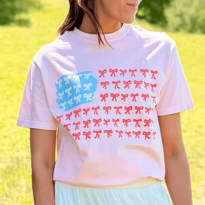 American Flag Bows Tee featuring a pastel pink shirt with red and blue bow designs arranged in a flag pattern.