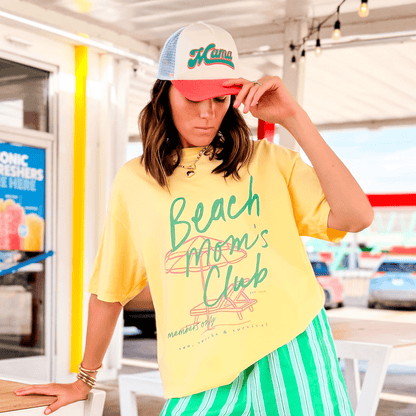 Mama ponytail hat in sherbert flowers design, worn by a woman with brown hair, paired with a yellow shirt and striped gree...