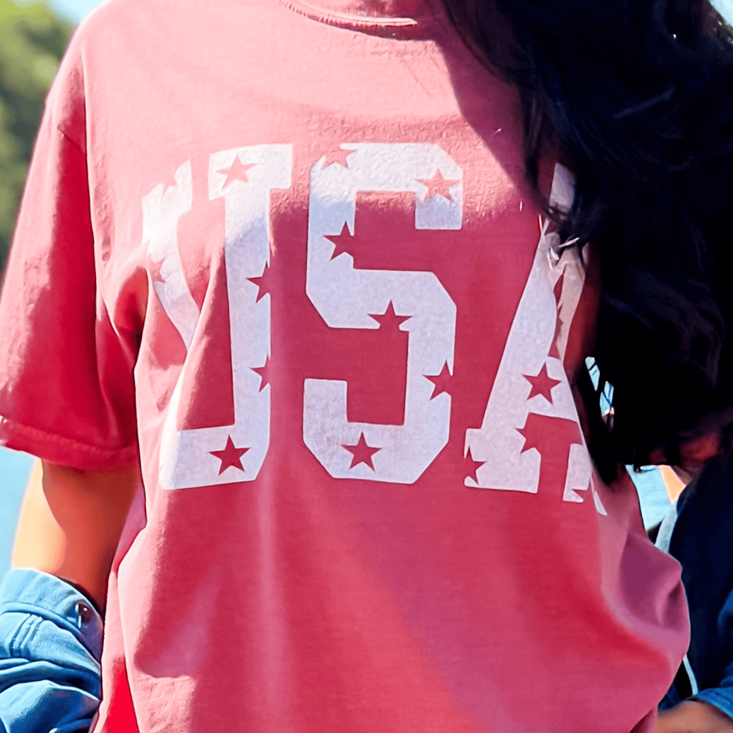 Distressed USA tee in brick red with white star and letter print, worn casually outdoors.