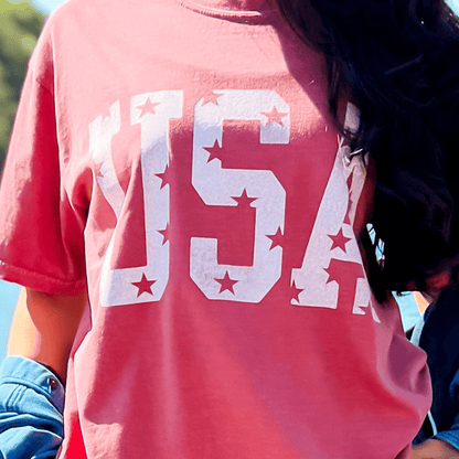 Distressed USA tee in brick red with white star and letter print, worn casually outdoors.