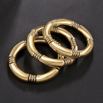 Gold tube stretch bracelet set featuring three interlinked bracelets with a shiny finish on a dark background.