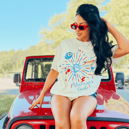 American Girlz tee with colorful graphic design, worn by a woman sitting on a red Jeep.