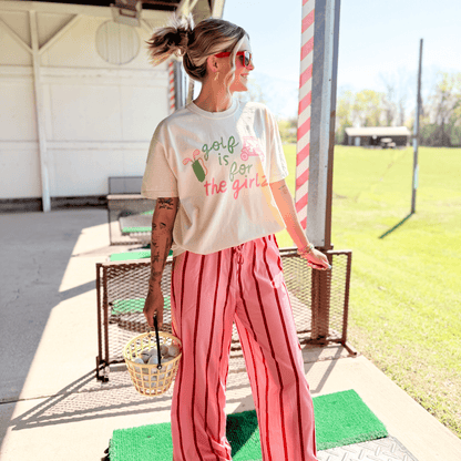 Woman wearing a t-shirt with text and pink pants standing on a golf green.