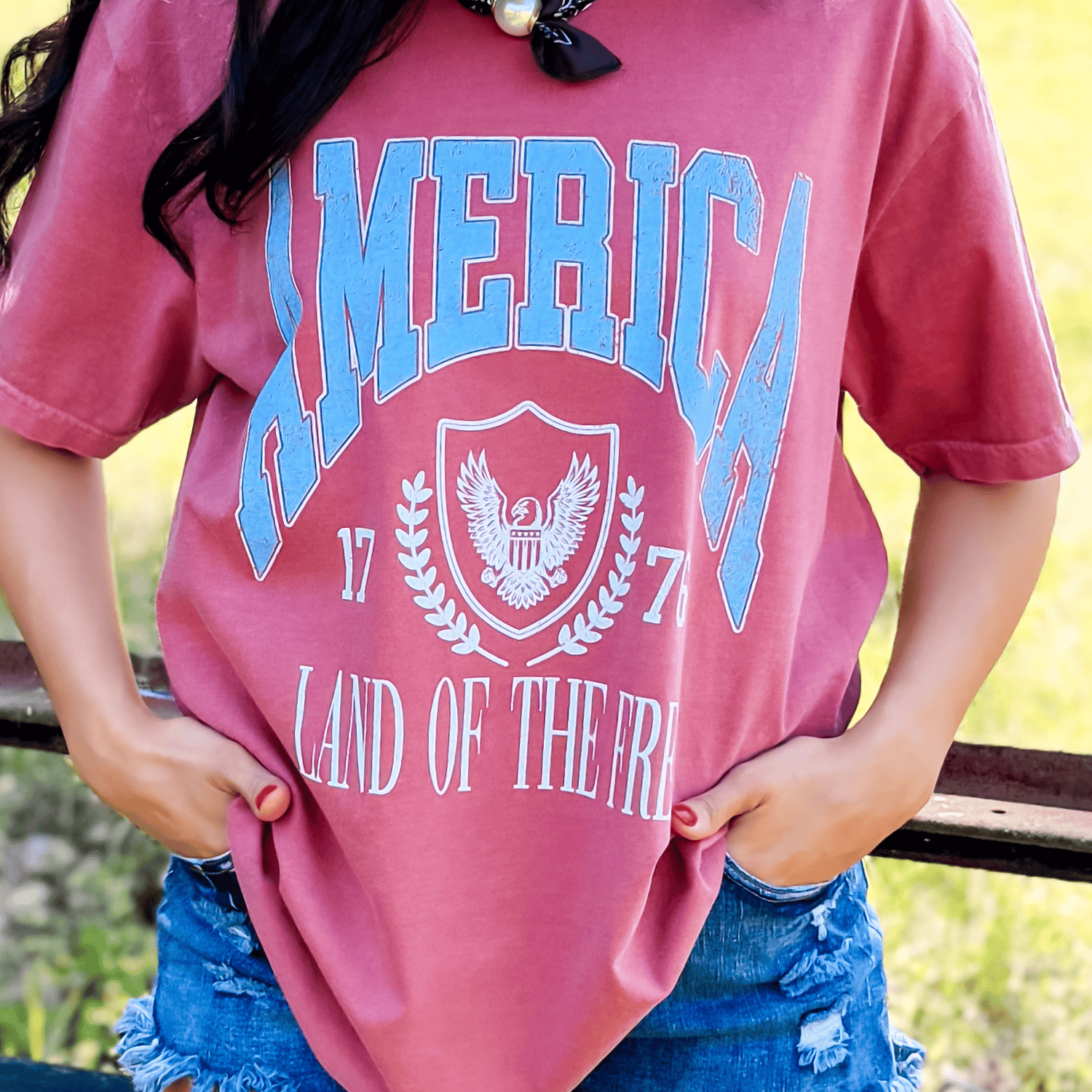 Land of the Free collegiate tee in dusty rose with blue lettering, featuring an eagle emblem and distressed details.
