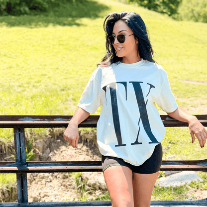 White State Initial Tee featuring a large "TX" graphic, worn with black shorts, against a green outdoor background.